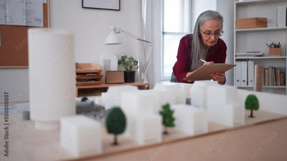 Senior woman eco architect with model of modern bulidings working in office. Senior woman eco architect with model of modern bulidings working in office.
