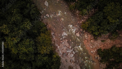 Aerial shot of a rocky river flowing between trees