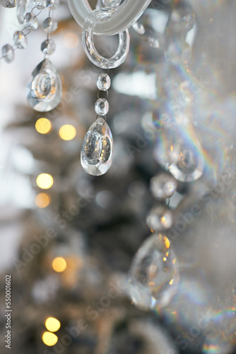 Close up of chandelier decorative crystal or glass pendants and christmas tree on background. Interior design. The concept of New year and Christmas.