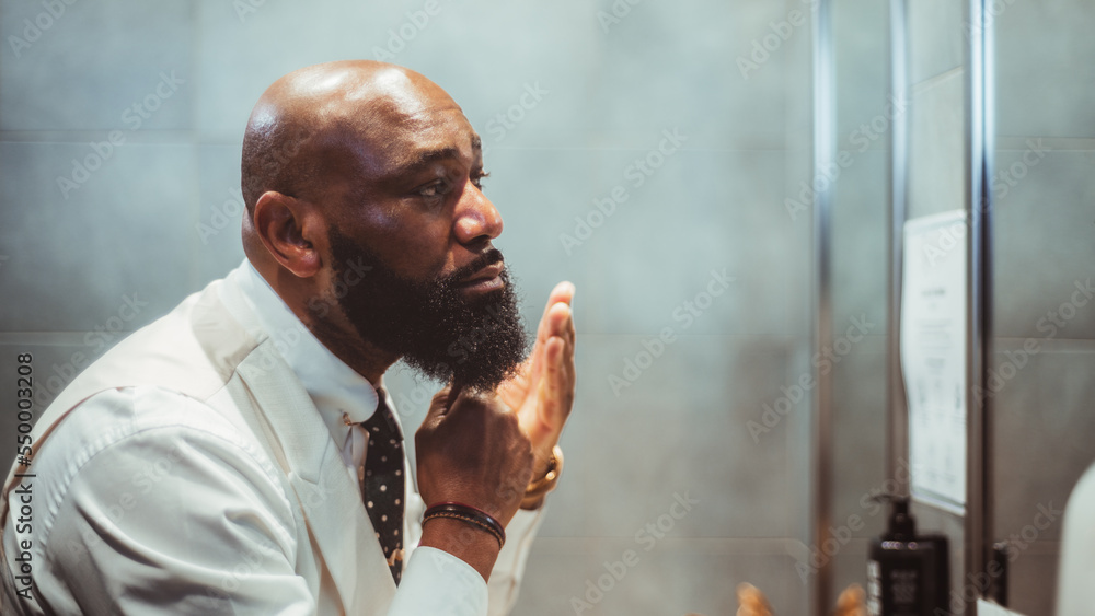A profile view of a handsome bald black man grooming, brushing, and ...