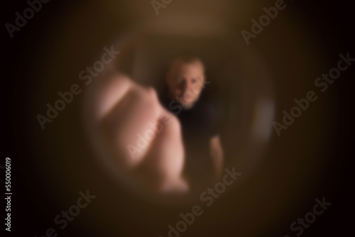 View from the peephole. Angry male neighbor knocking on the front door with his fist, close-up. Blurred photo