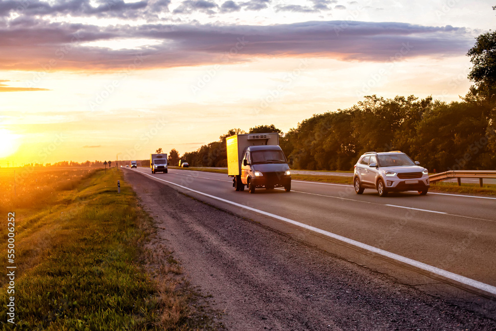 A van transports cargo on a motorway in the summer against the backdrop of a sunny sunset in the evening. The concept of cargo transportation on vans, mobility and speed of cargo delivery. 