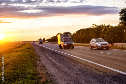 A van transports cargo on a motorway in the summer against the backdrop of a sunny sunset in the evening. The concept of cargo transportation on vans, mobility and speed of cargo delivery.  © HENADZY