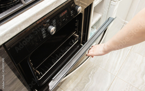 A woman's hand opens the door of a modern electric oven in the kitchen. Copy space for text
