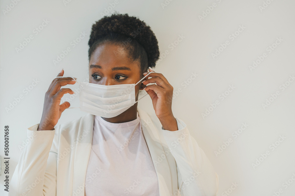 Portrait of smiling african woman taking off an facial mask while looking away isolated over white wall, indoors. Virus, epidemic, disease. Portrait of smiling african woman taking off an facial mask while looking away isolated over white wall, indoors. Virus, epidemic, disease.