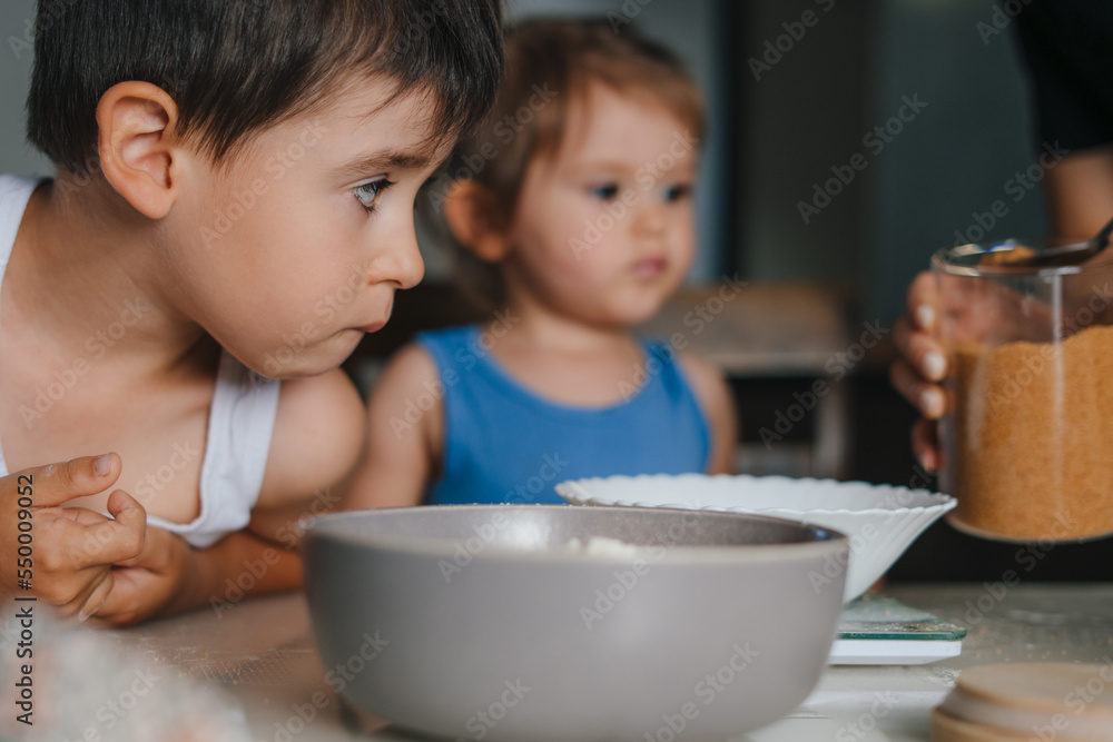 Two little caucasian kids learning to cook muffins at kitchen. Kids ready to mix ingredients, cooking cupcakes. Family education. Family home leisure. People Two little caucasian kids learning to cook muffins at kitchen. Kids ready to mix ingredients, cooking cupcakes. Family education. Family home leisure. People