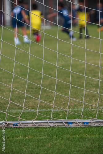 Close up of football goal net, seeing young soccer players during the match. Youth Soccer game on a sunny summer school tournament Day. Football match going on in a background.