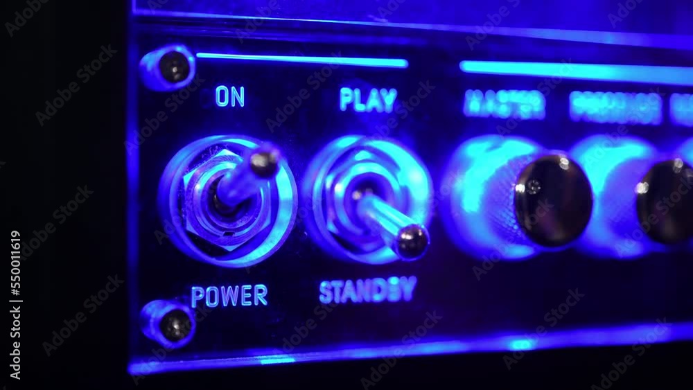 Power on electric equipment with blue glow light, human hand using analog toggle switch detail on music amplifier control panel