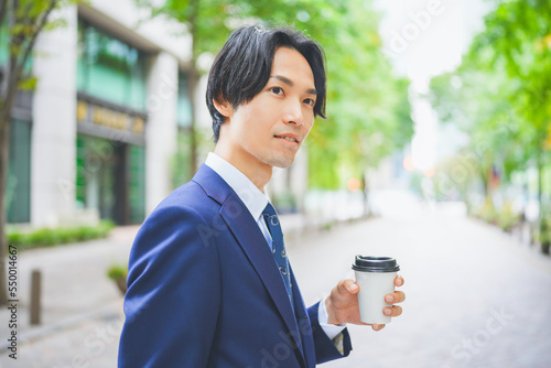 コーヒーを片手にオフィス街を歩くビジネスマン