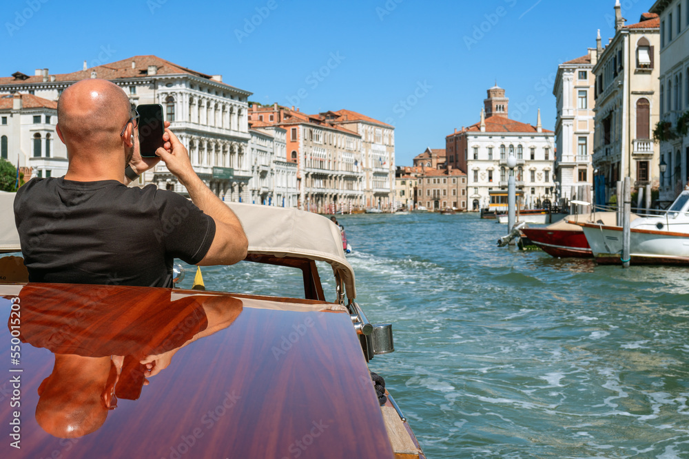 A young man holds a smartphone in his hands on the island of Venice in Italy on a sunny day while traveling by boat. Mobile communications while traveling, mobile photography and videography