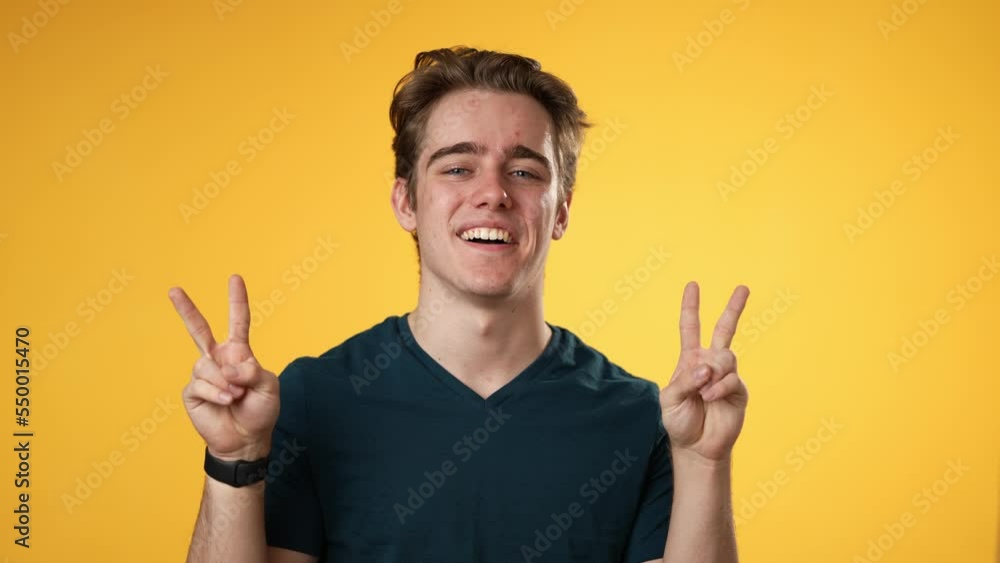 Portrait of happy young man 20s smiling and giving peace or victory sign gesture with hands isolated on solid yellow background. Portrait of happy young man 20s smiling and giving peace or victory sign gesture with hands isolated on solid yellow background.