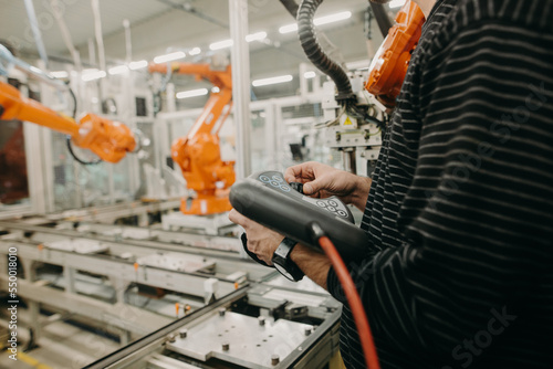 Technical engineer adjusting a robotic arm in the industrial automotive hall, industry concept
