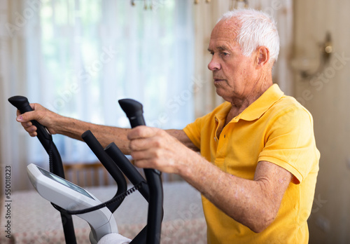 Elderly man exercising on elliptic trainer in living room