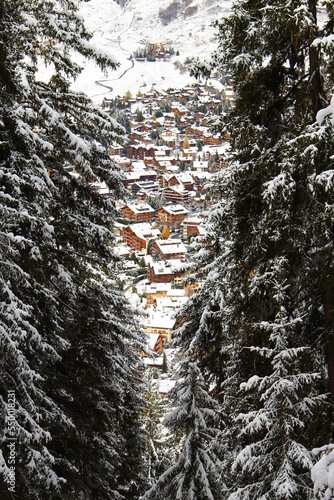 Verbier village. Traditional Alpine Village full of Swiss Chalets in the mountains. Seen between tall snow covered evergreens huddled in a mountain valley. Adorable winter travel Christmas concept 