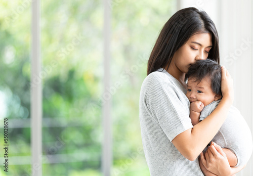 Portrait beautiful young Asian mother holding and hugging her newborn baby in living room. Healthcare and Happiness love asia woman lifestyle mother's day concept with copy space.	