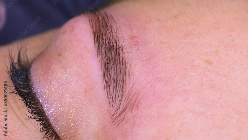 Close-up of the eyebrow of a model being combed with an eyebrow brush. Cosmetic procedure permanent eyebrow makeup. Eyebrow tattooing. Close-up of the eyebrow of a model being combed with an eyebrow brush. Cosmetic procedure permanent eyebrow makeup. Eyebrow tattooing.