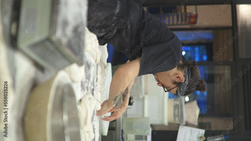 tattooed baker kneading bread doughs and placing the doughs with flour on the workbench of the bread workshop, vertical video tattooed baker kneading bread doughs and placing the doughs with flour on the workbench of the bread workshop, vertical video