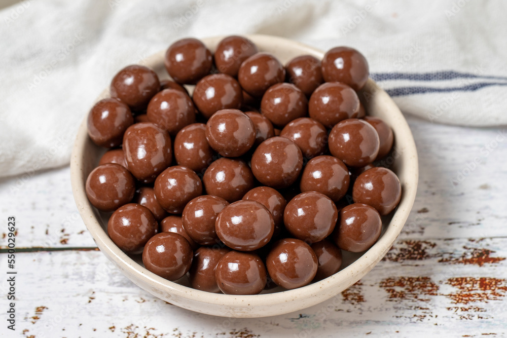 Chocolate coated hazelnut dragee. Hazelnut dragee chocolates on a white wood background. close up Chocolate coated hazelnut dragee. Hazelnut dragee chocolates on a white wood background. close up