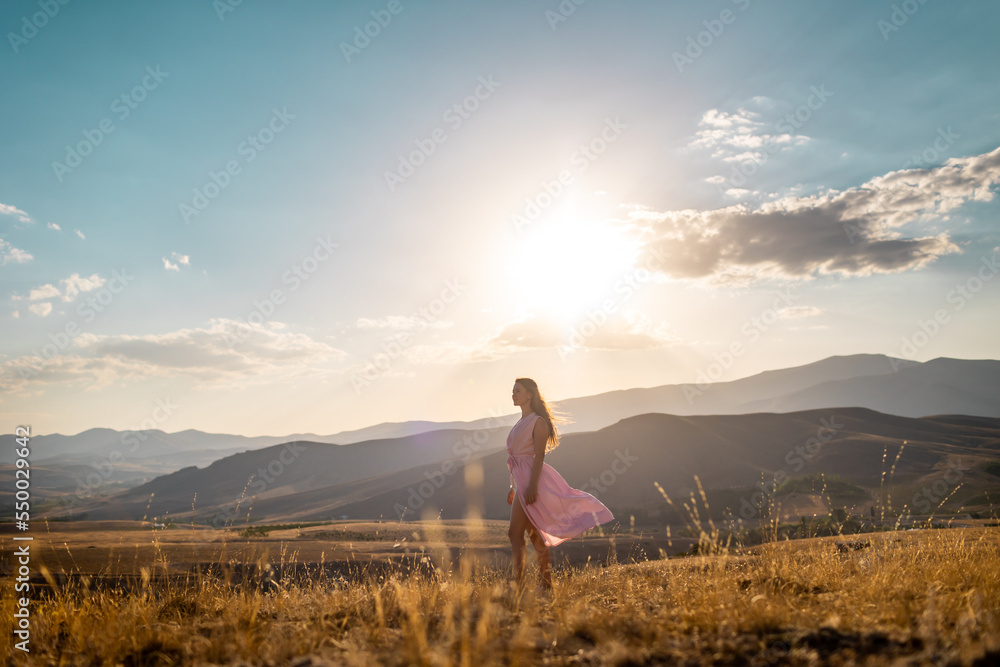 a girl in a pink dress walks across the field against the backdrop of mountains.