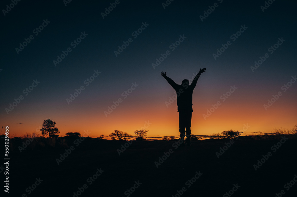 Silhouette im Abendrot - Kind reckt vor atemberaubender Sonnenuntergangskulisse seine Arme in den Himmel, Quiver tree Forest, Namibia