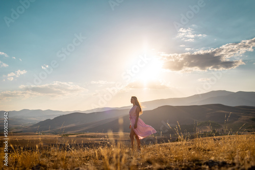 a girl in a pink dress walks across the field against the backdrop of mountains.