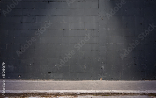 Frontal view of a black brick wall at night. In the foreground is a sidewalk illuminated by a cone of light. photo