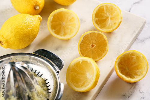 Pressing the lemon juice from many fresh yellow lemons manually, squeezed lemons on marble board