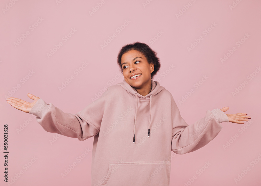 Smiling girl shrugging her shoulders. Young black woman in pink hoodie