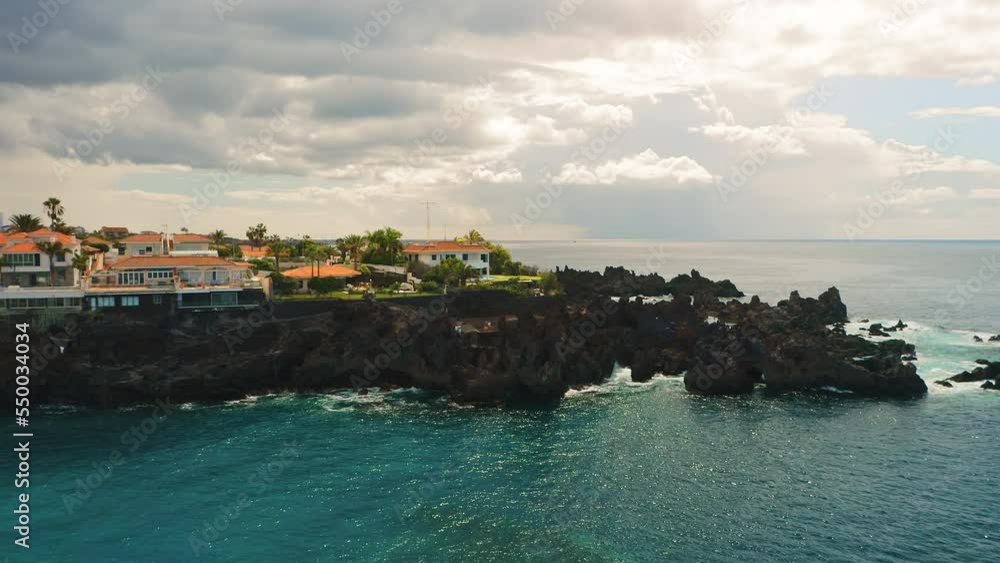 Aerial view of natural ocean coastline with pool on rocky volcanic beach of Devil in Tenerife Canary Island. Charco El Diablo. Black frozen lava flows volcanic bizzare stones. Resort town cityscape. Aerial view of natural ocean coastline with pool on rocky volcanic beach of Devil in Tenerife Canary Island. Charco El Diablo. Black frozen lava flows volcanic bizzare stones. Resort town cityscape.