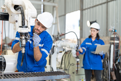 Male engineer repairing robot arm welding machine while female engineer checking and testing robot arm system in industrial factory. Team of technician in uniform working at factory workshop.