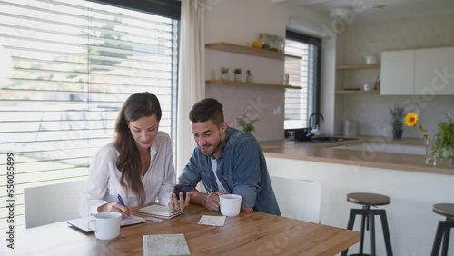 Young couple at home, using mobile phone for planning of finances.