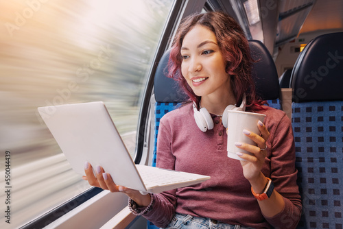 Obraz na płótnie Happy young girl rides in a modern intercity train and remotely via Wi Fi Internet works or studies or watches a movie and drinking coffee w salonie