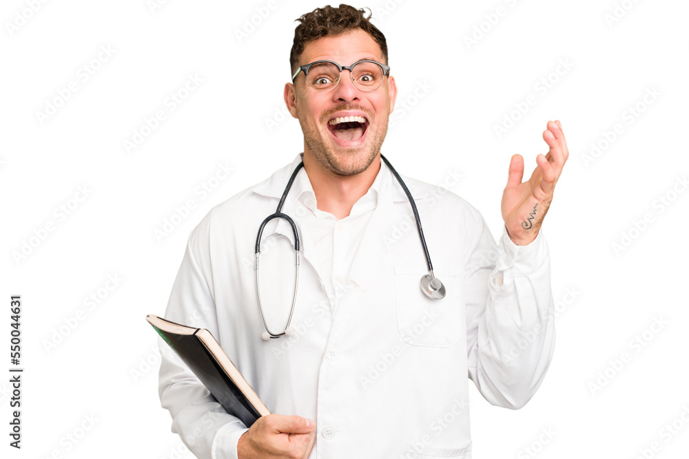 Young doctor caucasian man holding a book isolated receiving a pleasant surprise, excited and raising hands. Young doctor caucasian man holding a book isolated receiving a pleasant surprise, excited and raising hands.
