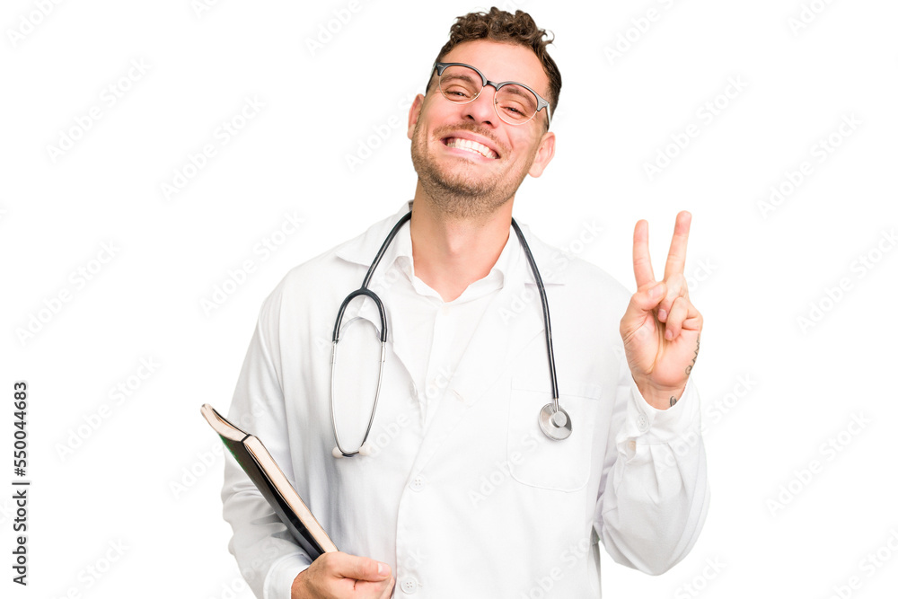Young doctor caucasian man holding a book isolated joyful and carefree showing a peace symbol with fingers. Young doctor caucasian man holding a book isolated joyful and carefree showing a peace symbol with fingers.