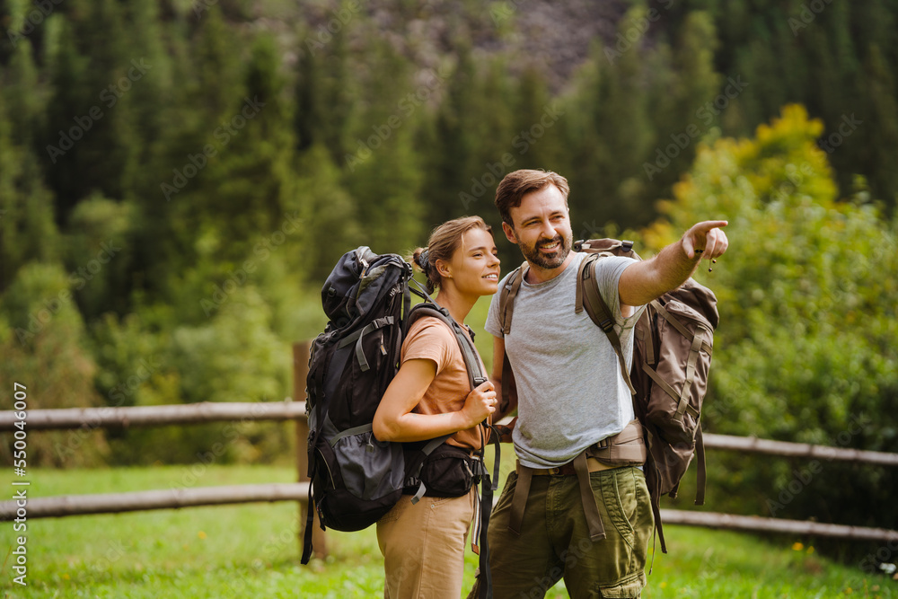 White young couple with backpacks hiking in green forest White young couple with backpacks hiking in green forest
