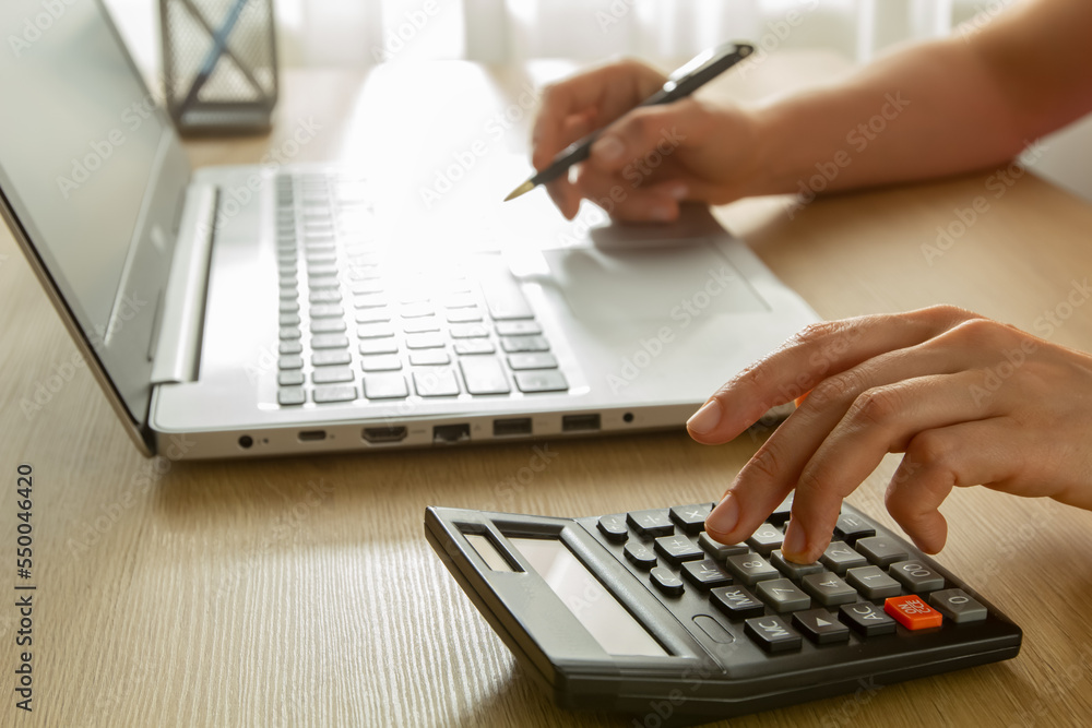 A woman is counting using a laptop and a calculator. A woman is counting using a laptop and a calculator.