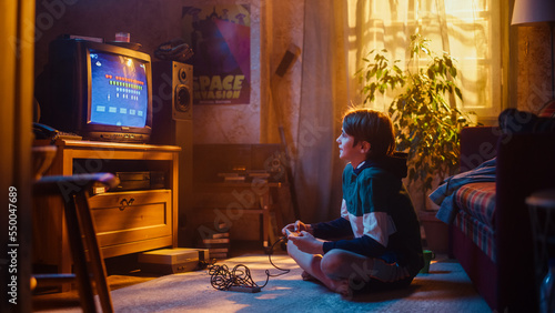 Young Boy Playing Eighties Eight Bit Arcade Space Shooter Video Game on a Console at Home in His Vintage Room with Old-School Interior. Child Successfully Wins the Level. Nostalgic Retro Childhood.