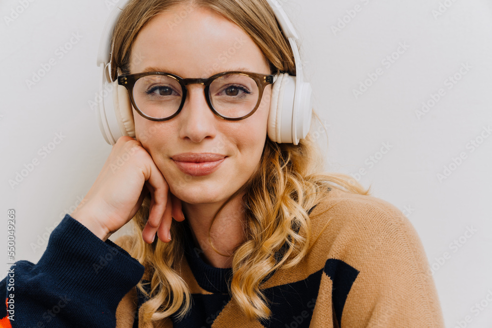 Young woman in headphones looking at camera isolated over white wall Young woman in headphones looking at camera isolated over white wall
