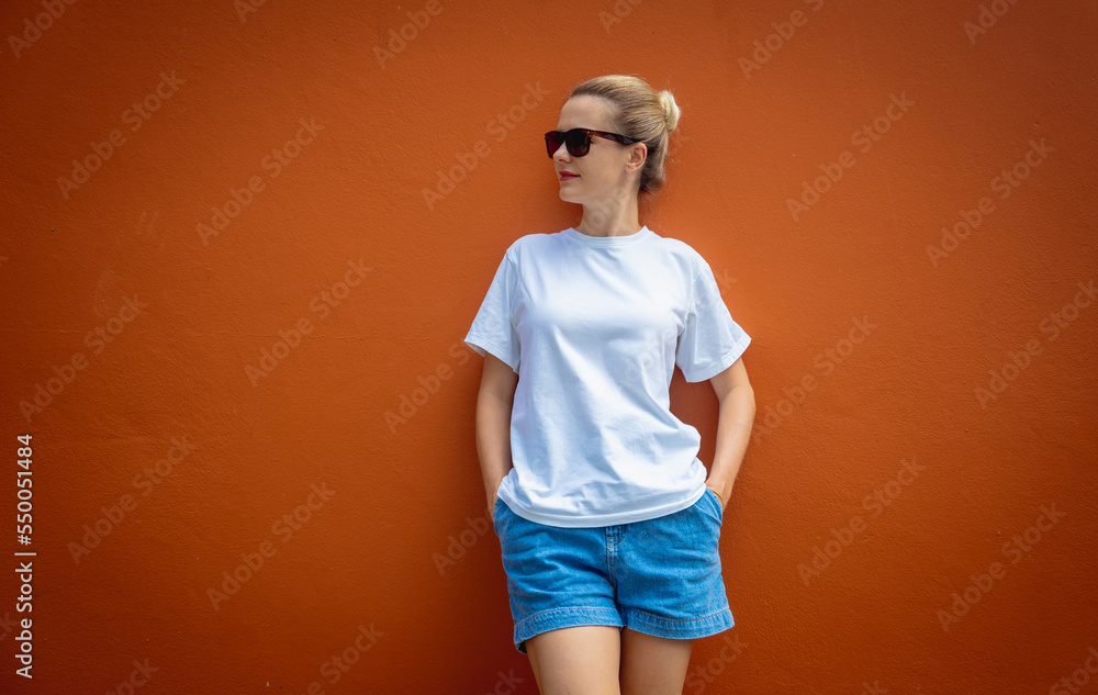 Female model wearing white blank t-shirt on the background of an orange wall. Female model wearing white blank t-shirt on the background of an orange wall.