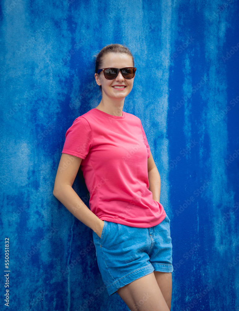 Female model wearing pink blank t-shirt on the background of an blue wall.