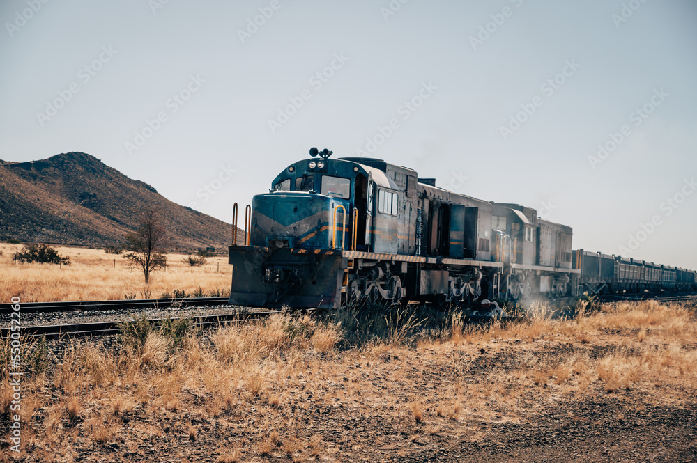 Naklejka premium Ein alter nostalgischer verstaubter Diesel Lok Güterzug fährt durch den Süden von Namibia