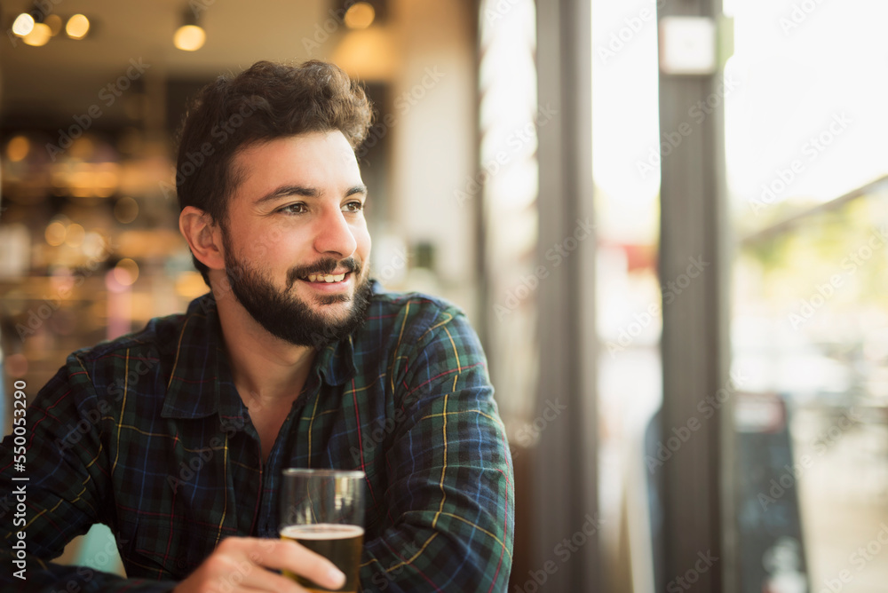 Bearded man in bar near to window drinking beer Bearded man in bar near to window drinking beer