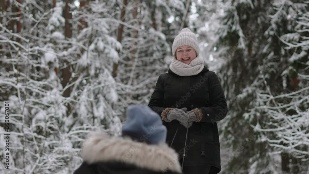 Young happy caucasian mother in warm clothes rolls son on sled in beautiful snowy forest among fir trees. Woman smiles, waves her hand in mittens and enjoys family vacation together, slow motion. Young happy caucasian mother in warm clothes rolls son on sled in beautiful snowy forest among fir trees. Woman smiles, waves her hand in mittens and enjoys family vacation together, slow motion.