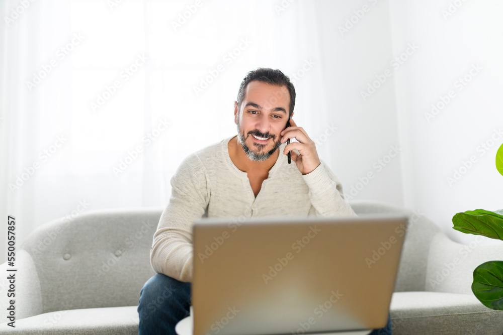 man with black hair using laptop at home sofa and talking to his cellphone man with black hair using laptop at home sofa and talking to his cellphone