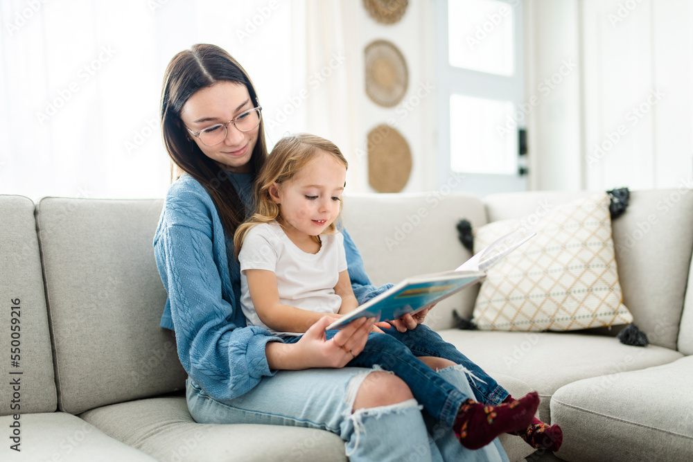 happy kid sitting on sofa with babysitter teen holding book