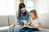 happy kid sitting on sofa with babysitter teen holding book