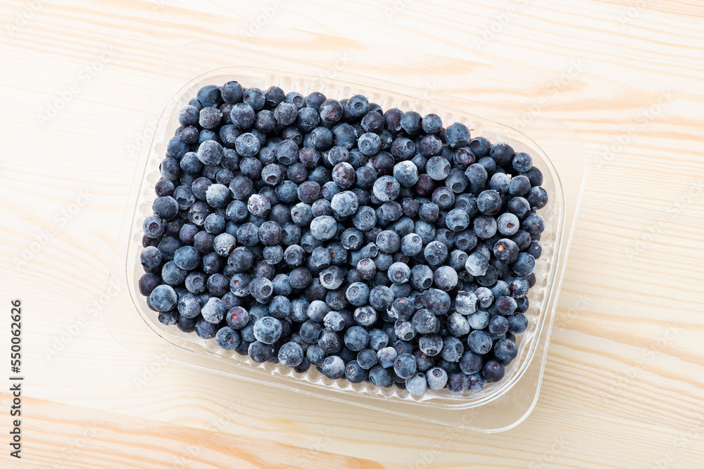 A lot of big ripe blueberries in plastic bowl on a white wooden table. Healthy nutrition, vitamins, natural food, tasty snack from wild forest A lot of big ripe blueberries in plastic bowl on a white wooden table. Healthy nutrition, vitamins, natural food, tasty snack from wild forest