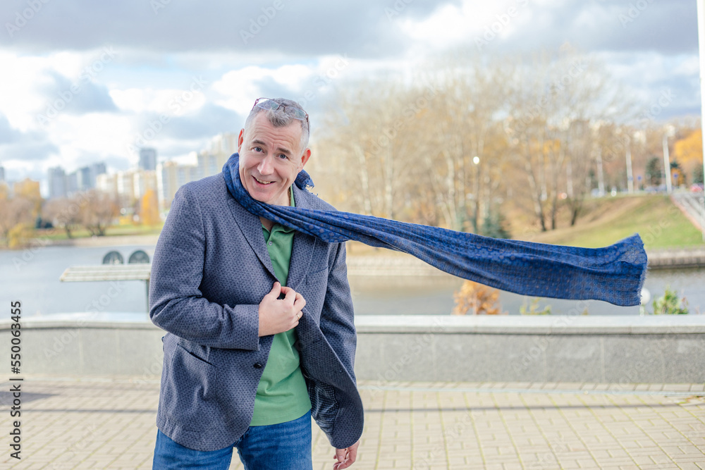 Portrait of happy middle-aged man with short hair wearing grey jacket,  flying blue scarf standing near concrete parapet. Stock Photo | Adobe Stock
