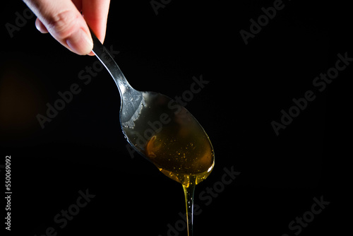 Close-up of honey dripping  from spoon on a black background. Copy space. photo