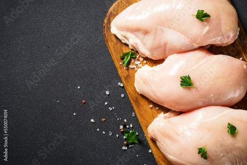 Chicken breast with spices at wooden cutting board on black background. Top view with copy space.